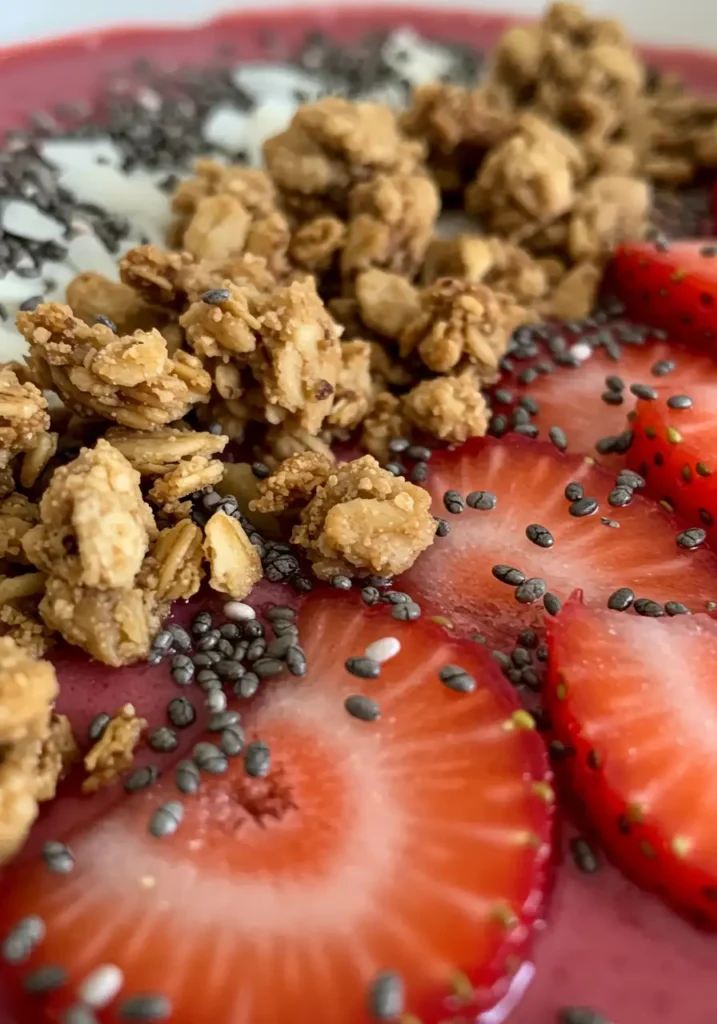The Best Healthy Strawberry Smoothie Bowl 6 Close-up of granola, chia seeds, and strawberry toppings on smoothie bowl.